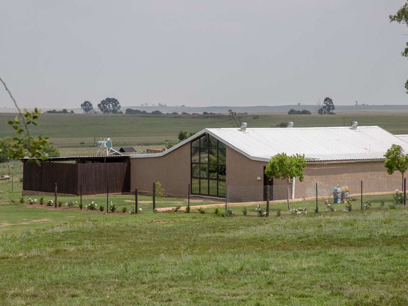 A rear view of a modern farm building featuring a large glass gable window, corrugated metal roof, and a fenced garden area.