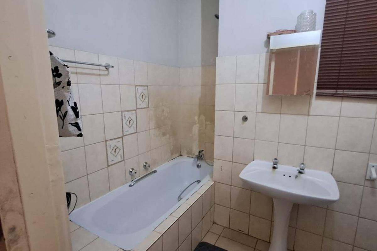 A dated bathroom featuring a standard bathtub, pedestal basin, and tiled finishes, currently requiring maintenance and cosmetic updates.