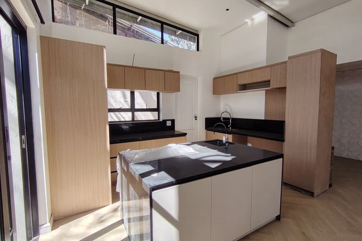 Modern kitchen featuring a central island, sleek light wood cabinetry, black stone countertops, and high clerestory windows providing ample natural light.