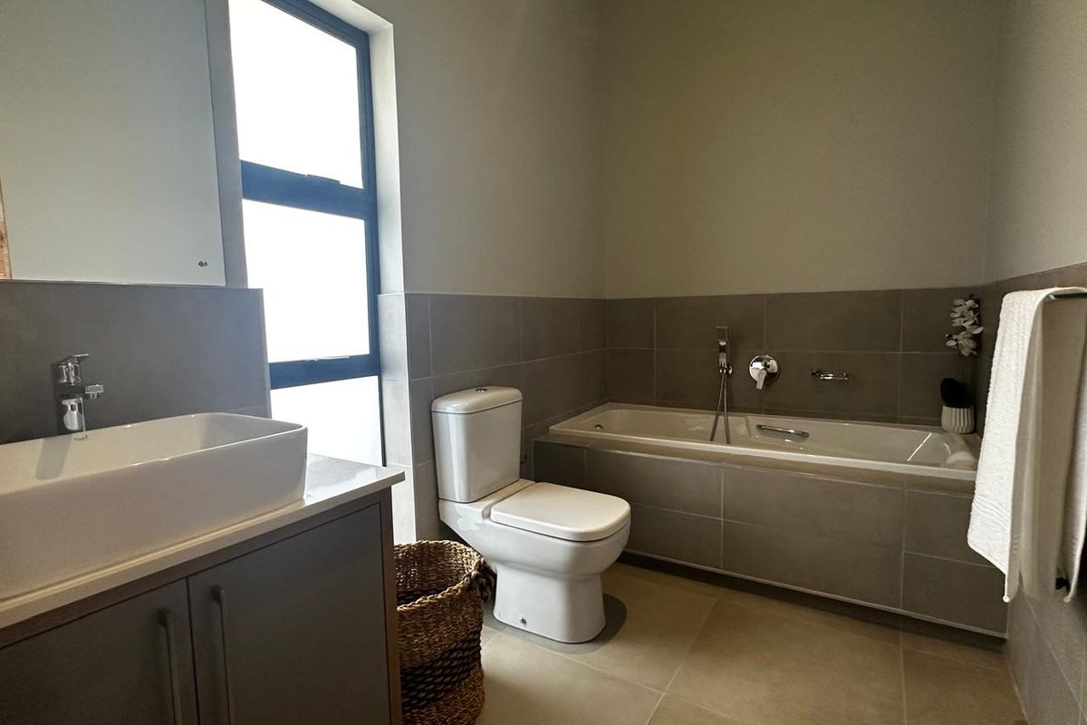A modern bathroom featuring a built-in bathtub, a contemporary vanity with a vessel sink, and neutral floor-to-ceiling tiling.