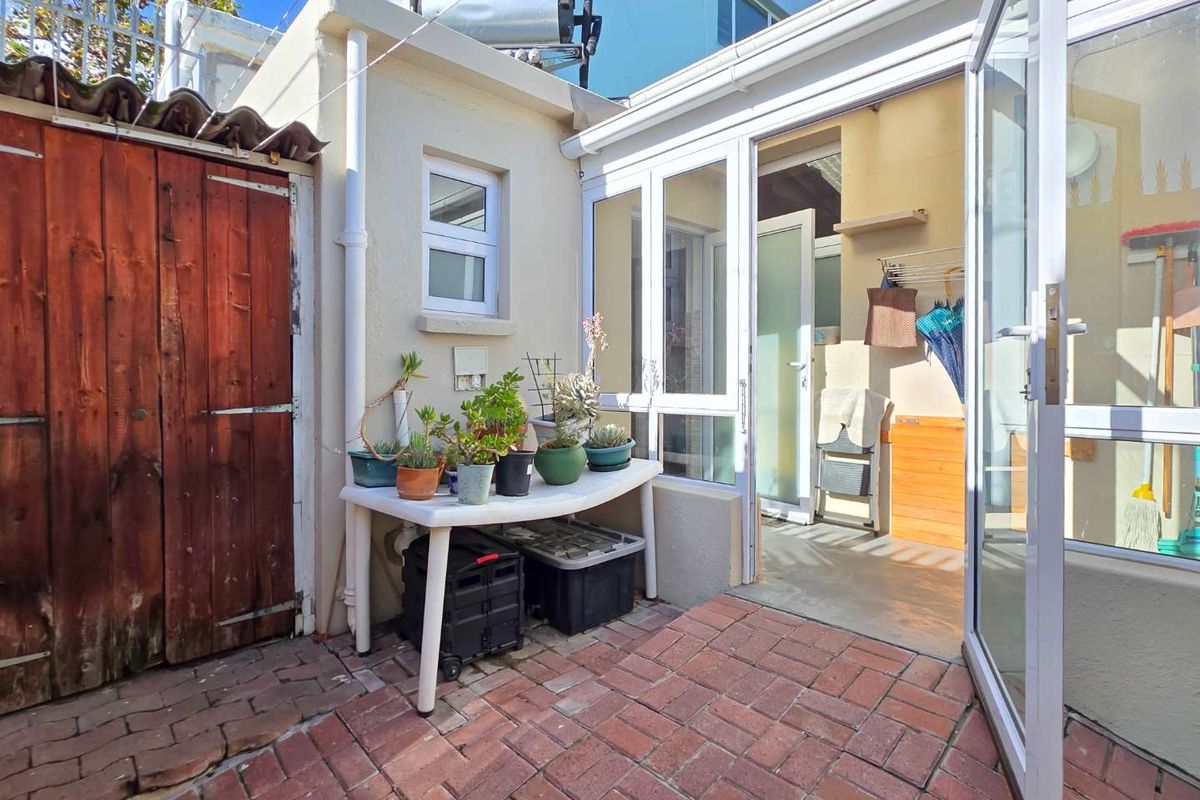 A paved rear courtyard area featuring a timber gate, solar water heater, and access to the interior through aluminium framed glass doors.