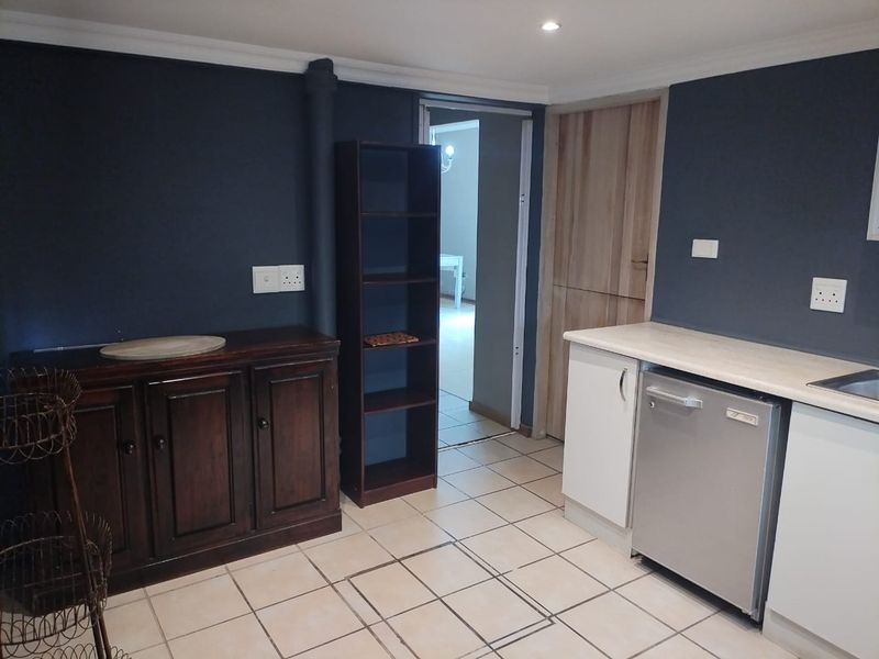 A functional kitchen area featuring tiled flooring, built-in cabinetry with laminate countertops, and an integrated dishwasher, leading into an adjacent room.