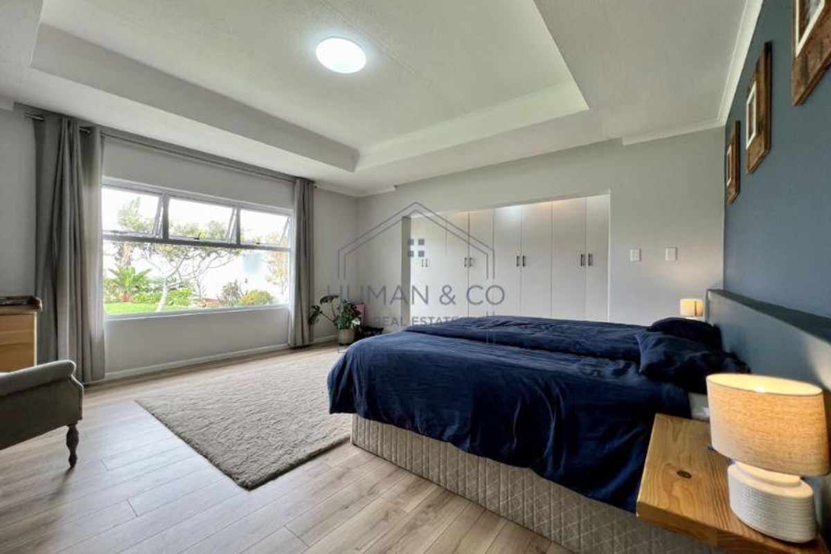 Spacious bedroom featuring a tray ceiling, large windows with garden views, and extensive built-in cabinetry for storage.
