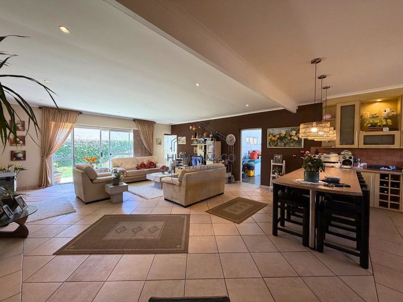 Spacious open-plan living and kitchen area featuring tiled flooring, recessed lighting, and a large kitchen island, with direct access to the garden through sliding doors.