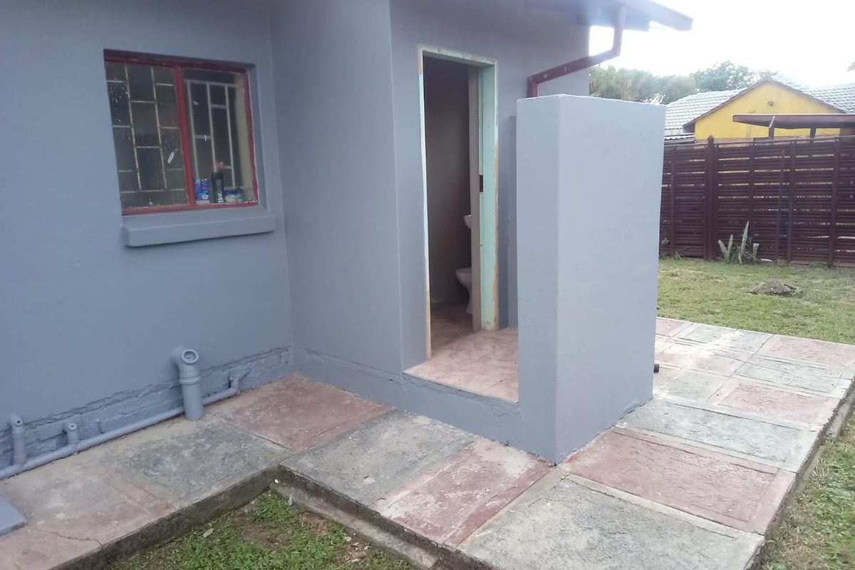 Rear exterior view showing a paved patio area, external access to a bathroom, and painted masonry walls.