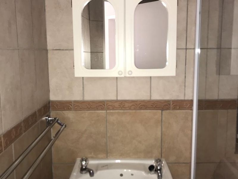 A functional bathroom featuring a pedestal basin, wall-mounted medicine cabinet, and a shower enclosure with tiled wall finishes.
