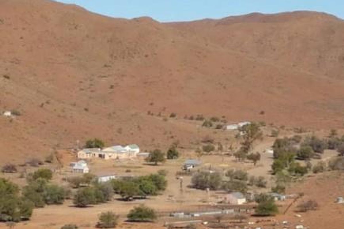 An aerial view of a rural farmstead nestled within a vast, arid mountainous landscape, featuring multiple outbuildings and surrounding natural terrain.