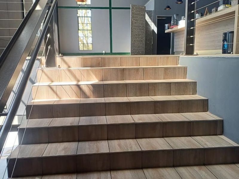 A modern entrance area featuring a wide tiled staircase with metal handrails and cable balustrades, set within an industrial-style space with exposed roof trusses.