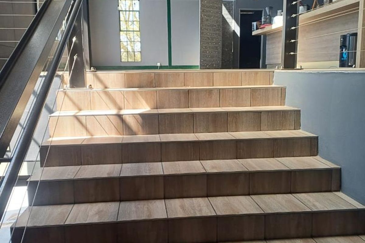 A modern entrance area featuring a wide tiled staircase with metal handrails and cable balustrades, set within an industrial-style space with exposed roof trusses.