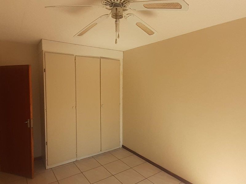 An empty bedroom featuring tiled flooring, built-in cupboards, and a ceiling fan, offering a neutral canvas for personalization.