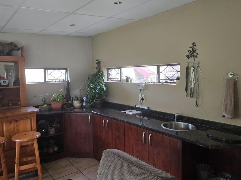 A functional kitchen area featuring dark wood cabinetry, granite countertops, a stainless steel sink, and tiled flooring with natural light from horizontal windows.