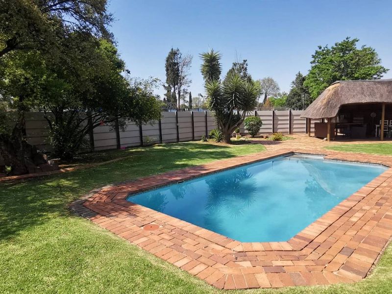 Outdoor entertainment area featuring a swimming pool with brick paving, a lawn, and a thatched lapa structure enclosed by a precast concrete boundary wall.