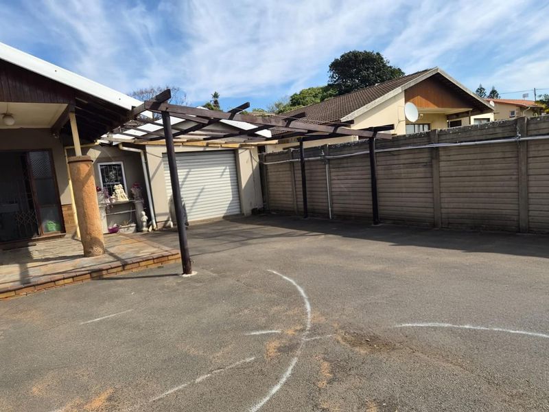 Rear exterior area featuring a paved driveway, a timber pergola structure, and a precast concrete boundary wall adjacent to the garage.