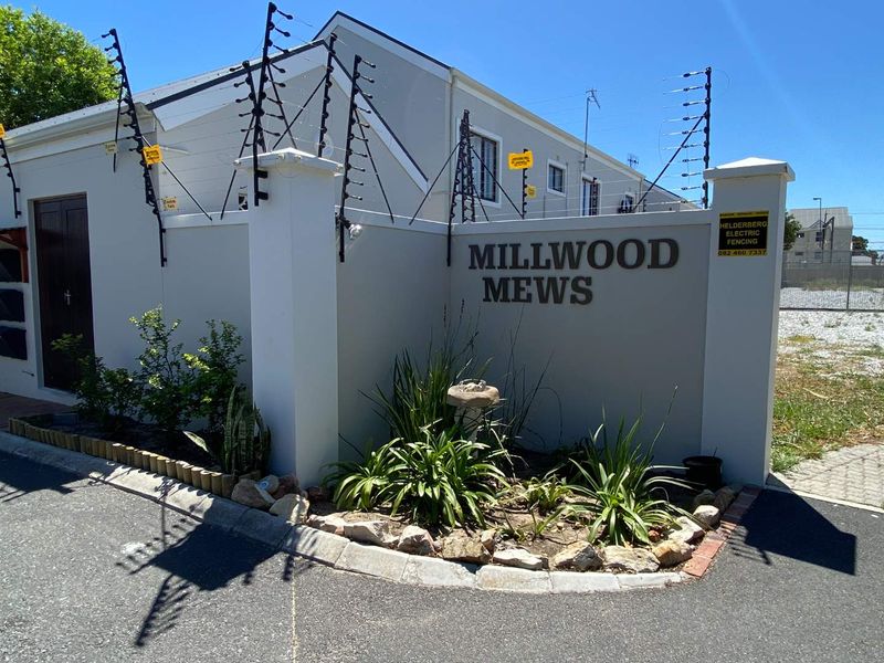 Front entrance view of Millwood Mews townhouse complex featuring a secure boundary wall with electric fencing and established garden landscaping.
