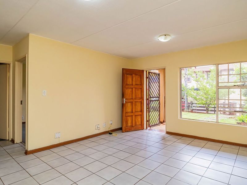 A bright, empty living room featuring neutral walls, tiled flooring, and a large window providing natural light and access to an outdoor area.