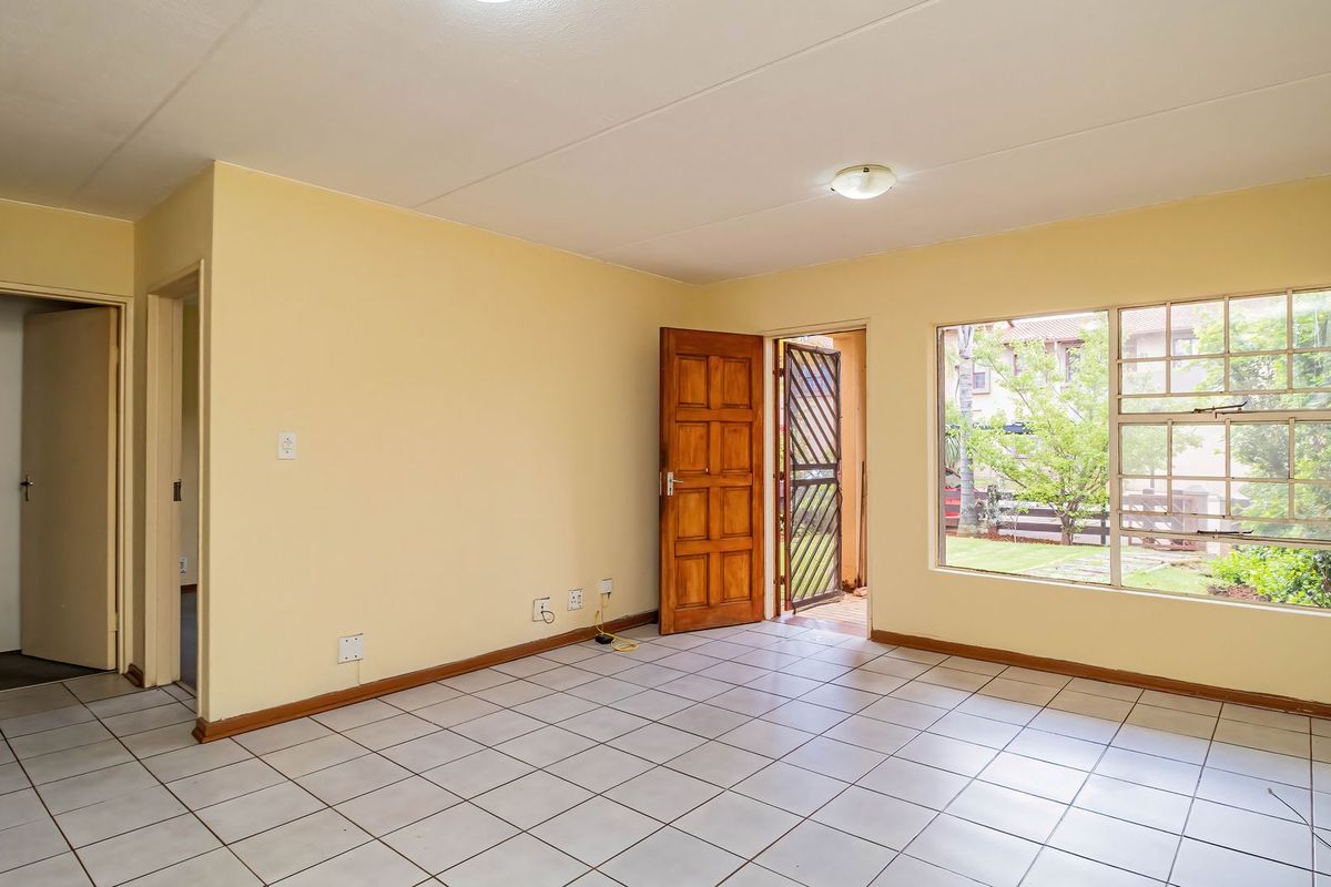 A bright, empty living room featuring neutral walls, tiled flooring, and a large window providing natural light and access to an outdoor area.