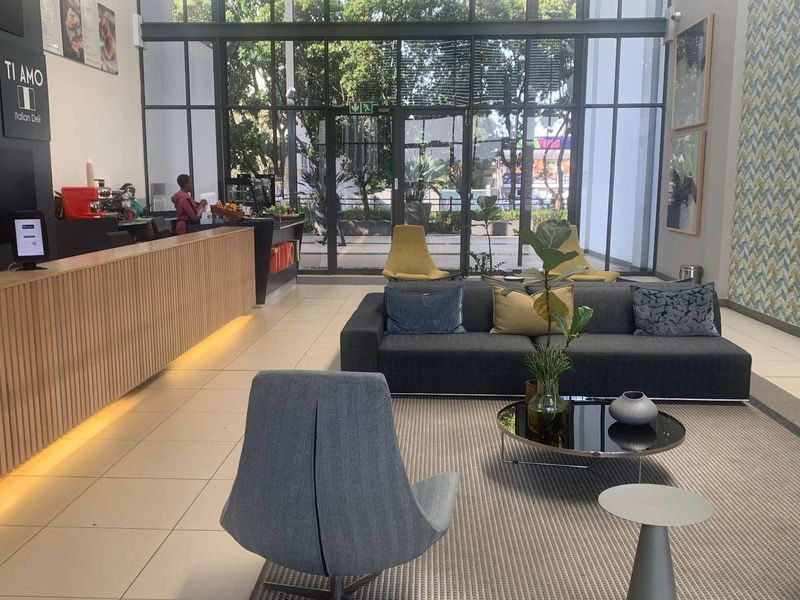 Modern open-plan office reception area featuring a sleek timber-slatted counter, expansive floor-to-ceiling glass windows, and contemporary tiled flooring.