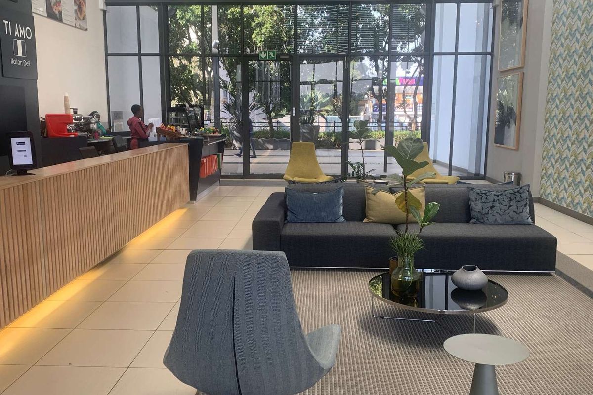 Modern open-plan office reception area featuring a sleek timber-slatted counter, expansive floor-to-ceiling glass windows, and contemporary tiled flooring.