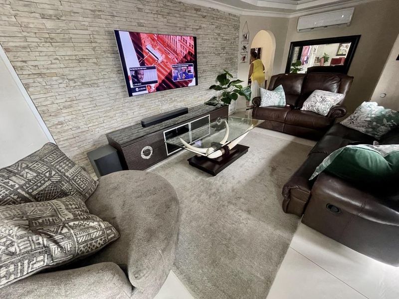 A comfortable living room featuring a textured stone veneer accent wall, split-system air conditioning, and neutral tiled flooring.