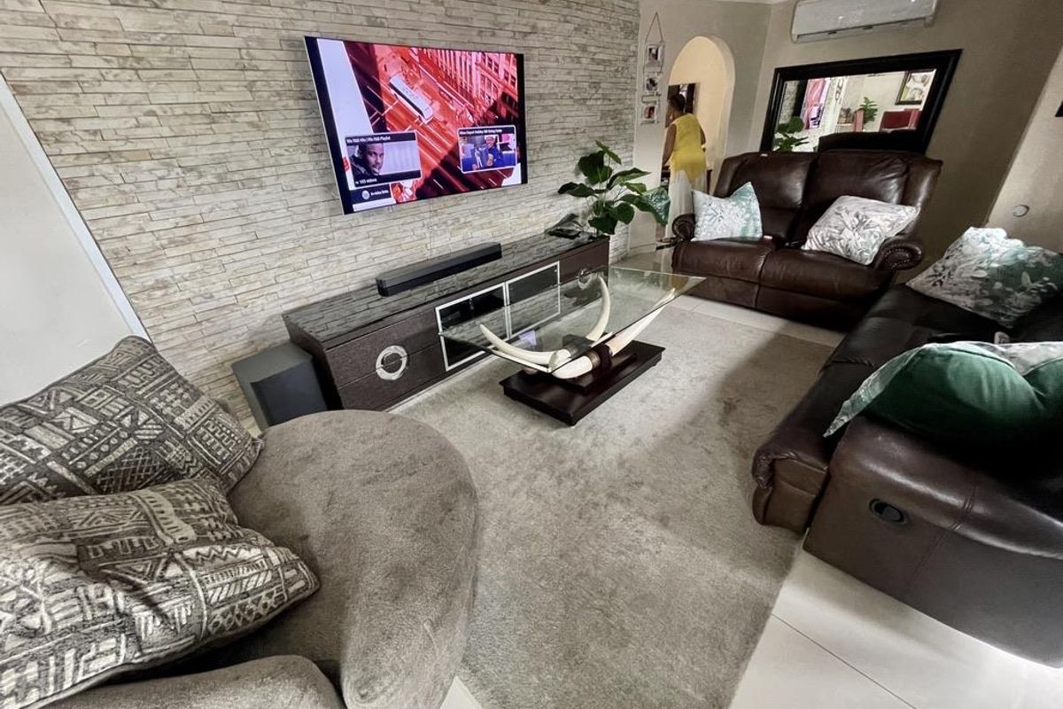 A comfortable living room featuring a textured stone veneer accent wall, split-system air conditioning, and neutral tiled flooring.