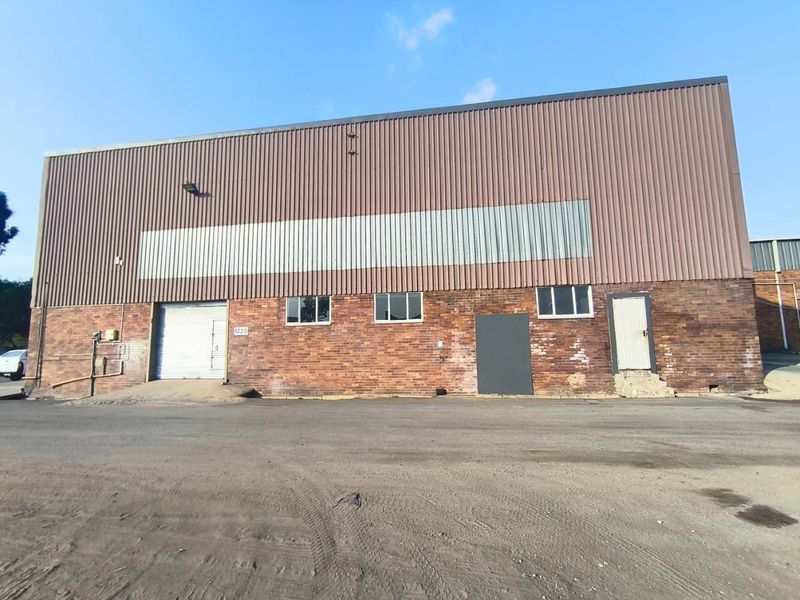 Industrial warehouse exterior featuring a combination of face brick and corrugated metal cladding with a roller shutter door and asphalt frontage.