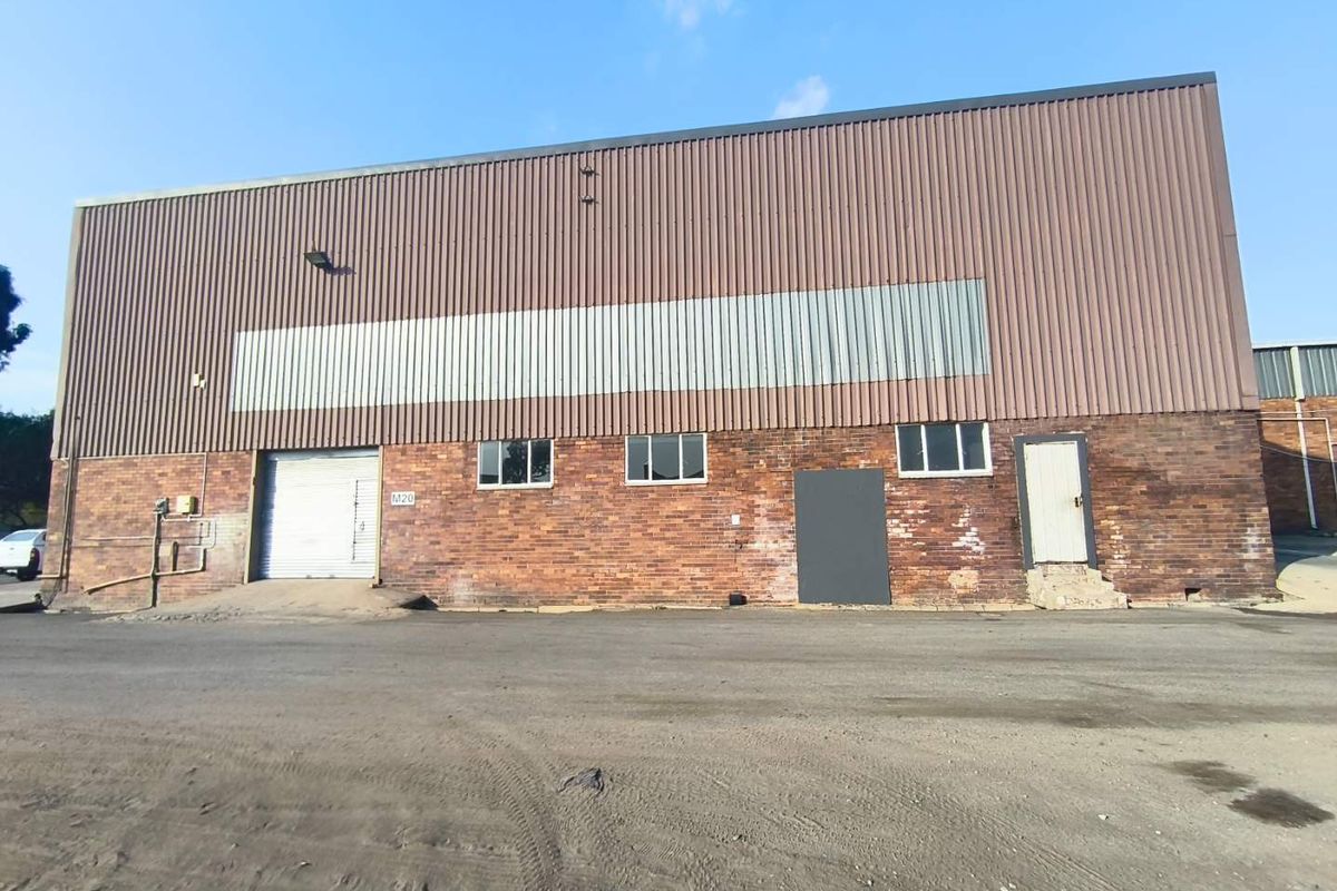 Industrial warehouse exterior featuring a combination of face brick and corrugated metal cladding with a roller shutter door and asphalt frontage.