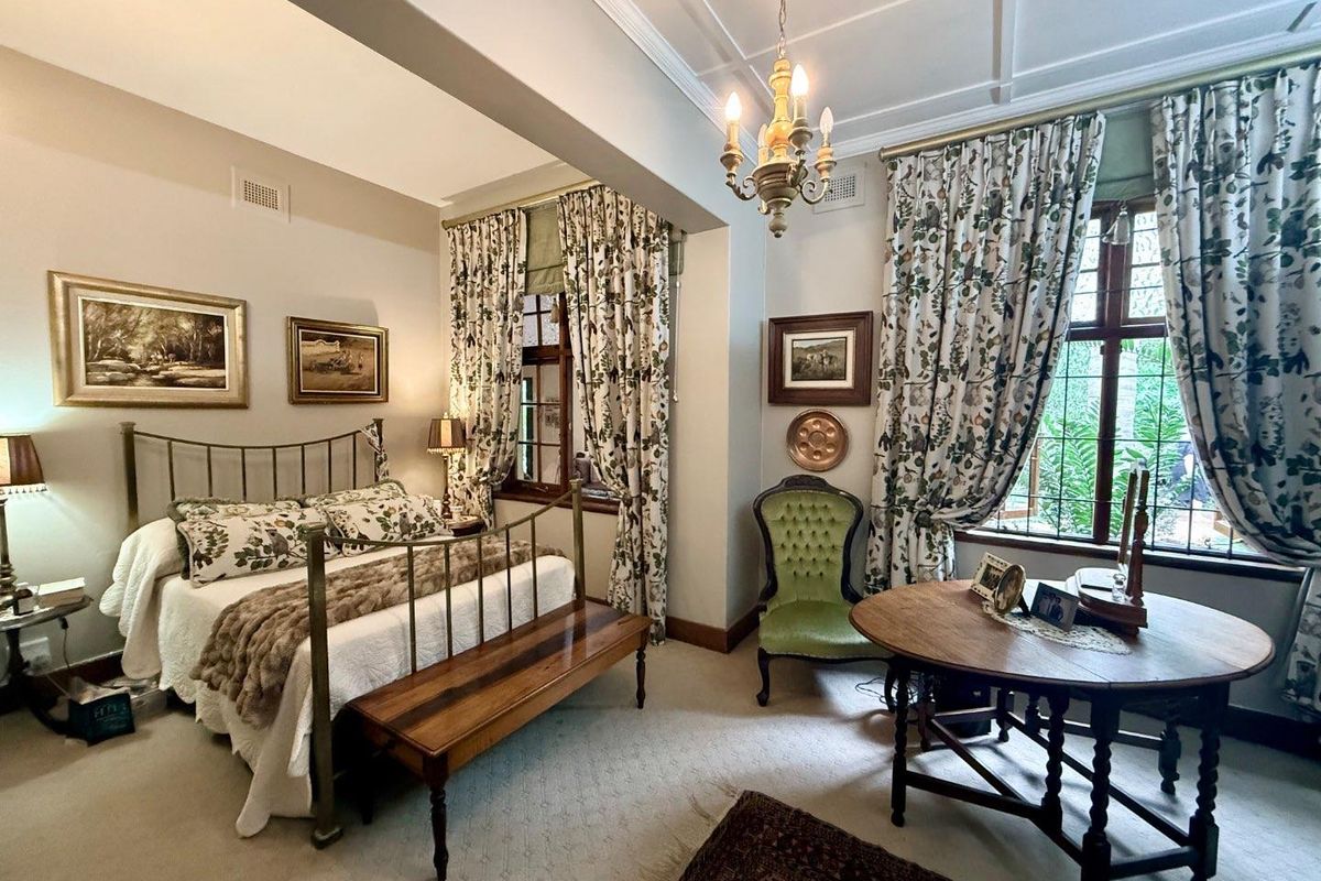 A spacious bedroom featuring high ceilings with decorative molding, large windows with garden views, and classic architectural detailing.