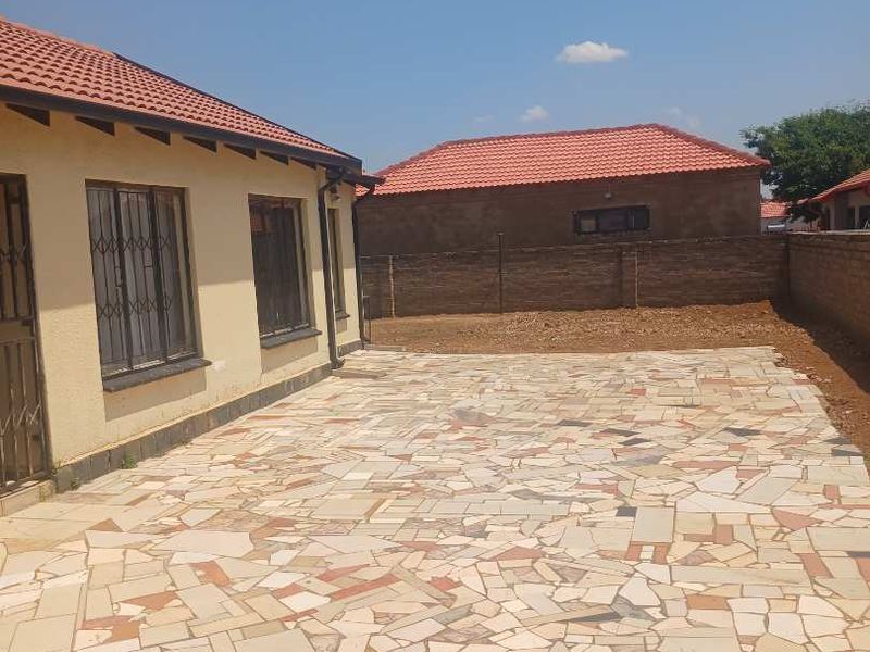 Rear exterior view featuring a large crazy paving patio area, tiled roof, and secure brick boundary walling.