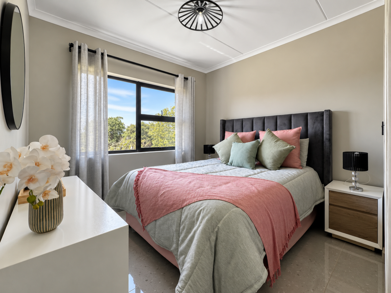 A well-maintained bedroom featuring tiled flooring, neutral wall tones, and a large window providing natural light and a pleasant outdoor view.