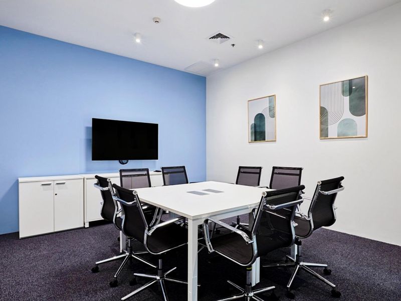 A modern, well-lit office meeting room featuring a central table, built-in storage cabinetry, and professional carpet flooring.