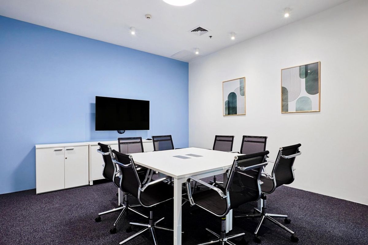 A modern, well-lit office meeting room featuring a central table, built-in storage cabinetry, and professional carpet flooring.