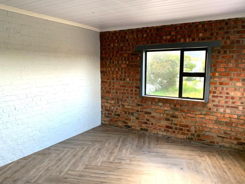 A bright, empty bedroom featuring a combination of exposed and painted brick walls, herringbone flooring, and a timber ceiling with an aluminium window.