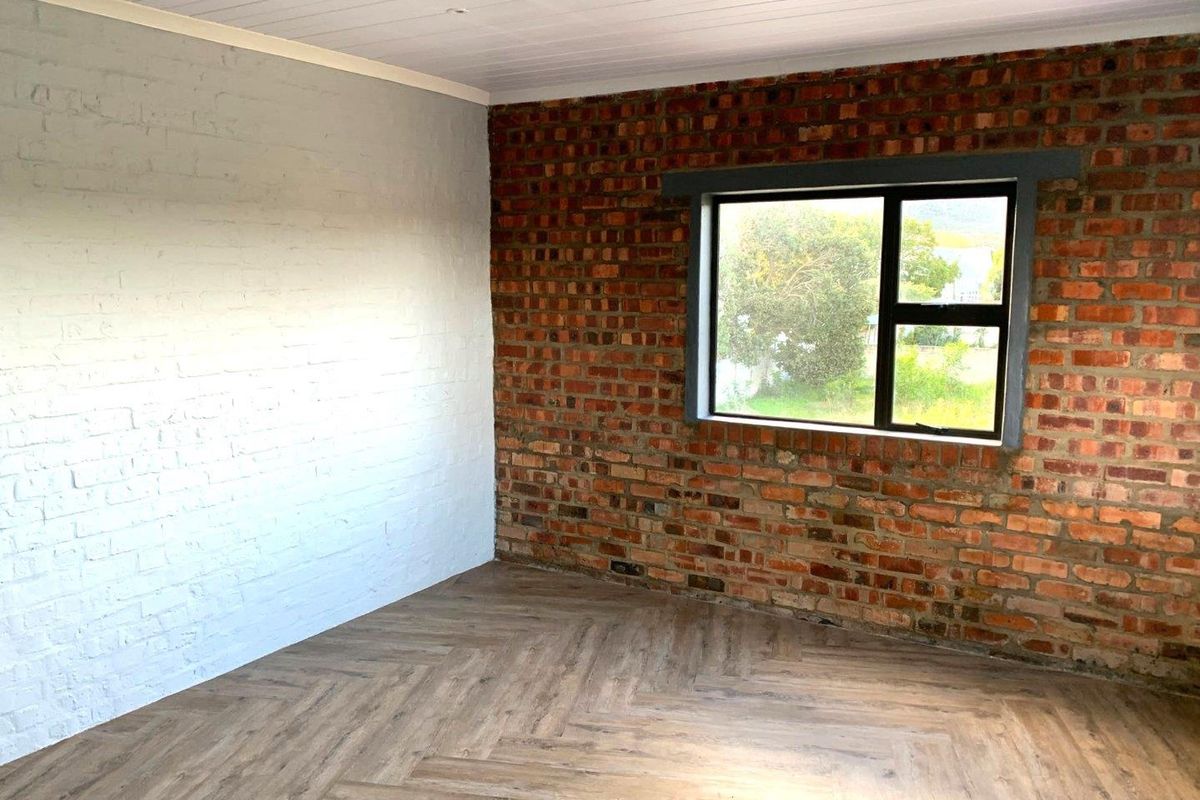 A bright, empty bedroom featuring a combination of exposed and painted brick walls, herringbone flooring, and a timber ceiling with an aluminium window.