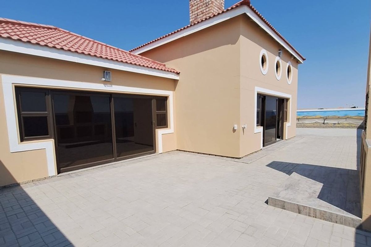 A spacious rear exterior view featuring a paved patio area, sliding glass doors, and a well-maintained building facade with a brick chimney.