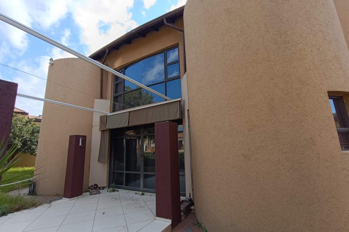 Rear exterior view of the property featuring a tiled patio area, large glass windows, and distinctive curved architectural wall elements.