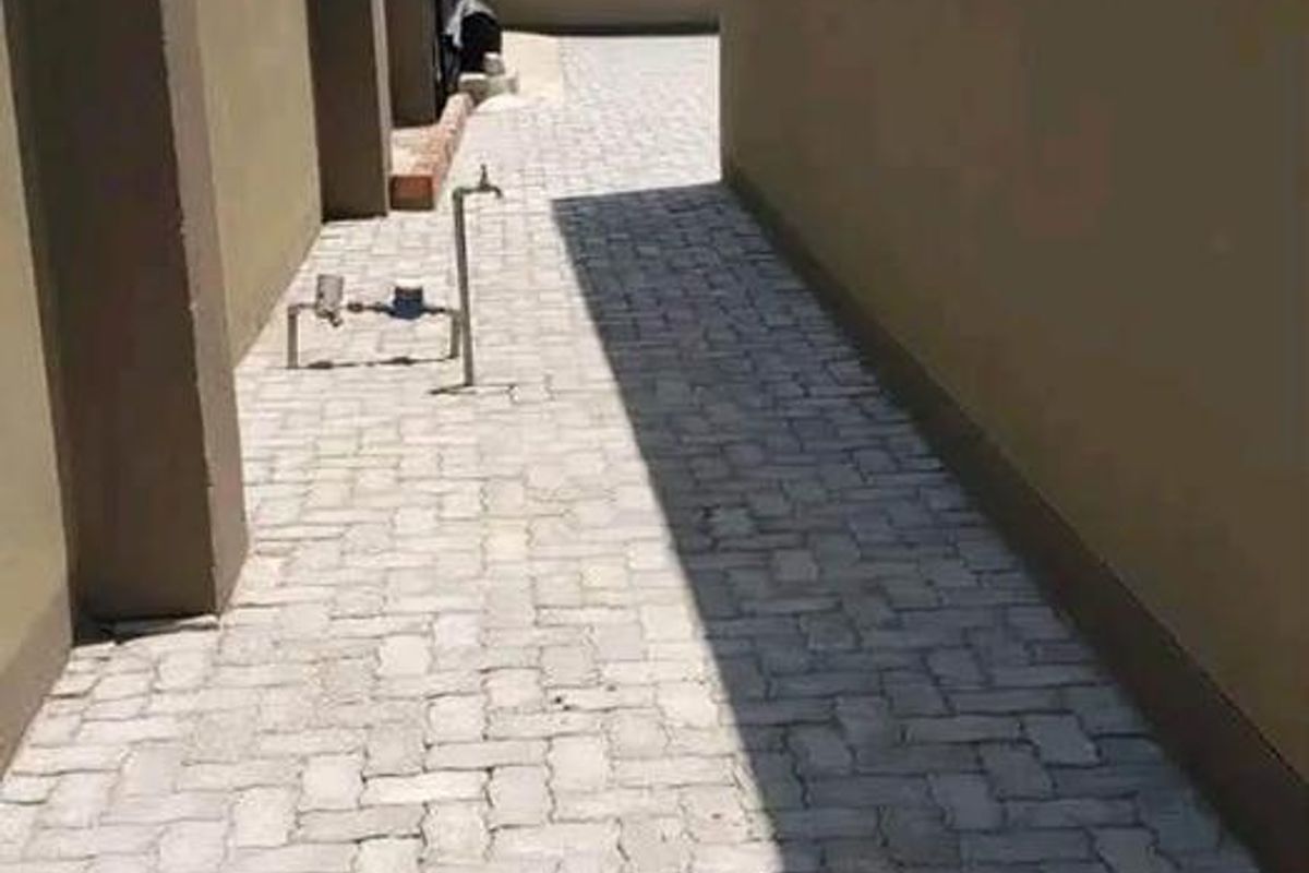 A side passage featuring paved flooring, boundary walls with electric fencing, and an external water tap.