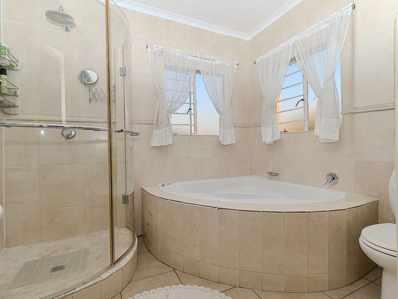 A functional bathroom featuring a corner bathtub, a separate curved glass shower enclosure, tiled finishes, and louvered windows for natural ventilation.