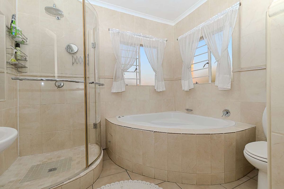 A functional bathroom featuring a corner bathtub, a separate curved glass shower enclosure, tiled finishes, and louvered windows for natural ventilation.
