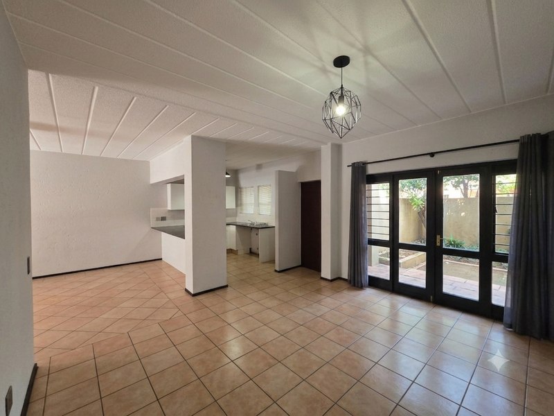 Spacious open-plan living and kitchen area featuring tiled floors, neutral walls, and direct access to a private outdoor patio through glass doors.