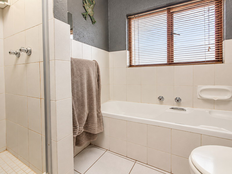 A functional bathroom featuring a separate shower enclosure, a built-in bathtub, tiled finishes, and a window with venetian blinds.