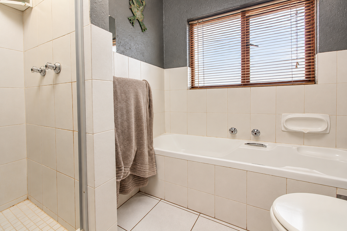 A functional bathroom featuring a separate shower enclosure, a built-in bathtub, tiled finishes, and a window with venetian blinds.