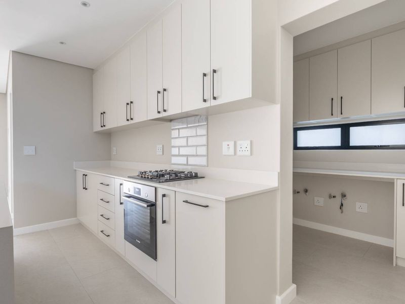Modern kitchen featuring sleek cabinetry, stone countertops, integrated gas hob, built-in oven, and a convenient adjoining scullery area with additional storage and plumbing.
