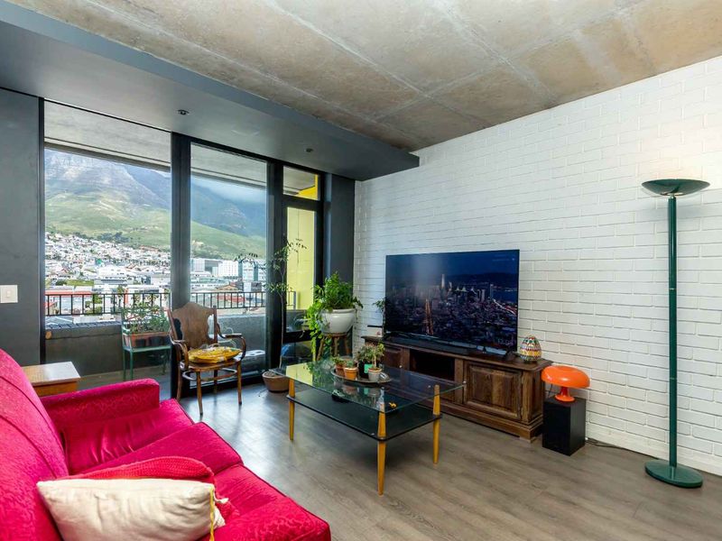 Modern living room featuring an exposed concrete ceiling, painted brick wall, and large sliding glass doors offering expansive mountain and city views.