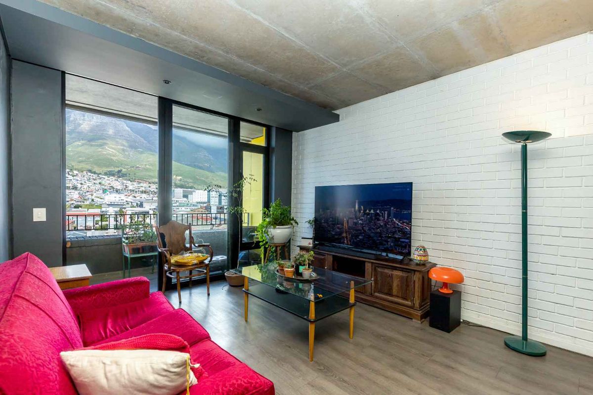 Modern living room featuring an exposed concrete ceiling, painted brick wall, and large sliding glass doors offering expansive mountain and city views.