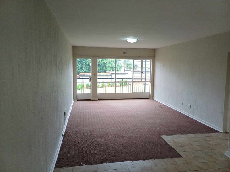 An empty, open-plan living area featuring carpeted flooring, a large glass sliding door with security gate, and neutral wall finishes.