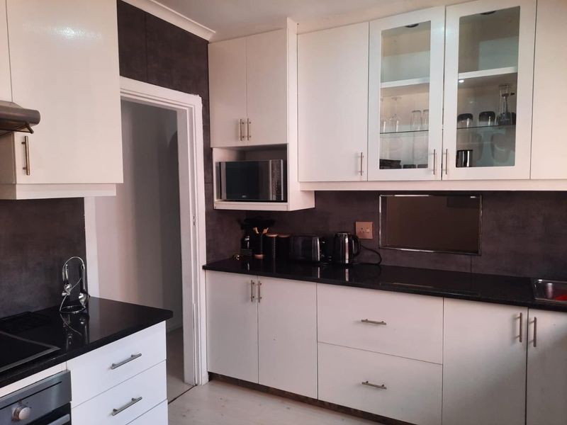 Modern kitchen featuring white cabinetry, contrasting dark granite countertops, built-in appliances, and glass-fronted display cabinets.