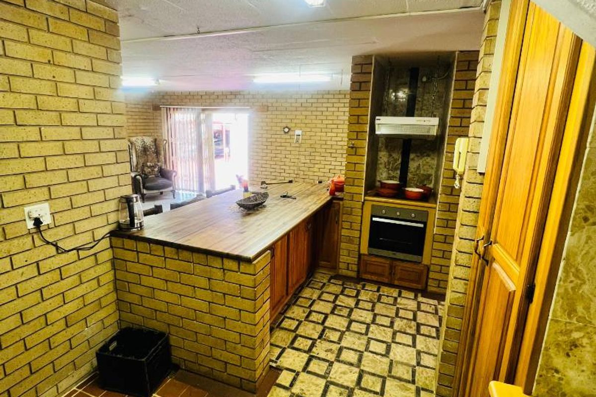 A dated kitchen area featuring brick construction, wood-look countertops, built-in oven, and extractor fan, with direct access to an adjacent living space.