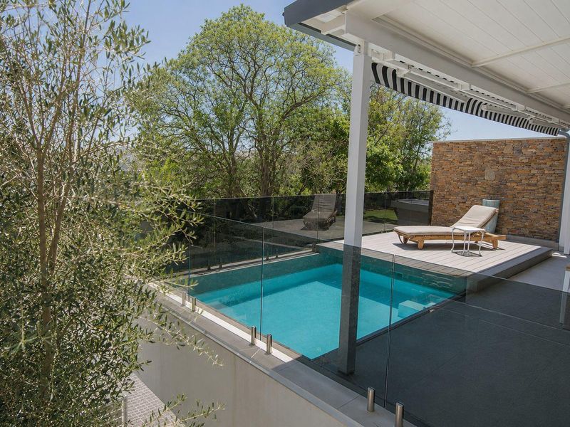 Modern outdoor entertainment area featuring a swimming pool, glass balustrades, timber decking, and a stone feature wall under a retractable awning.
