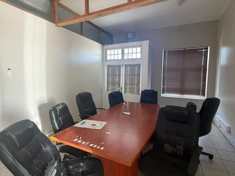 A functional office space featuring tiled flooring, a timber-framed glass partition, and natural light through window blinds.