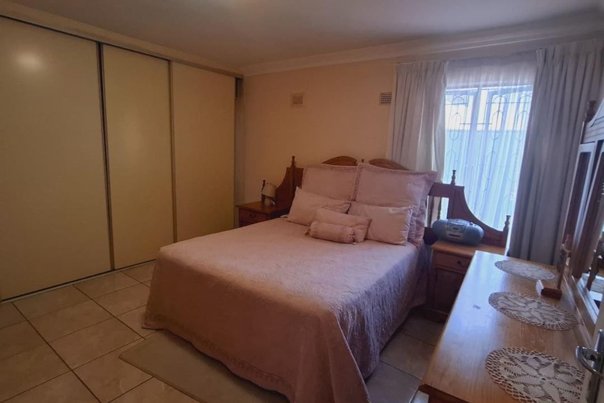 A functional bedroom featuring tiled flooring, a large built-in sliding wardrobe, and natural light through the window.